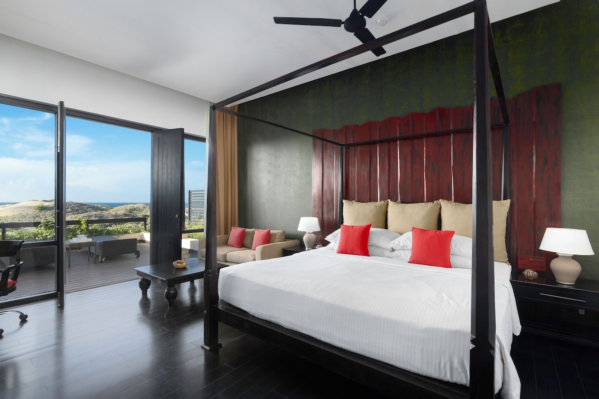 Un dormitorio espacioso con una cama grande, un balcón con mobiliario exterior y vistas a la ciudad.