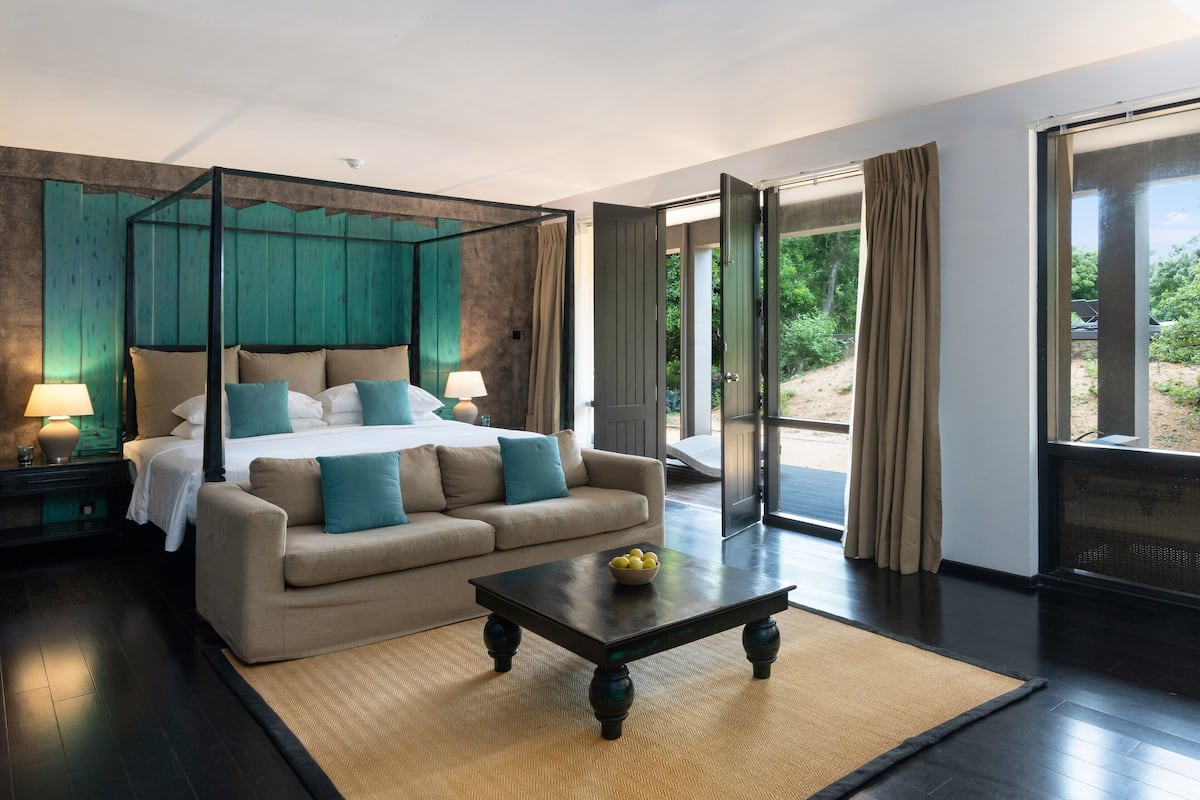 Un dormitorio con cama con dosel, un sofá, una mesa de centro y vistas al exterior a través de amplios ventanales correderas.