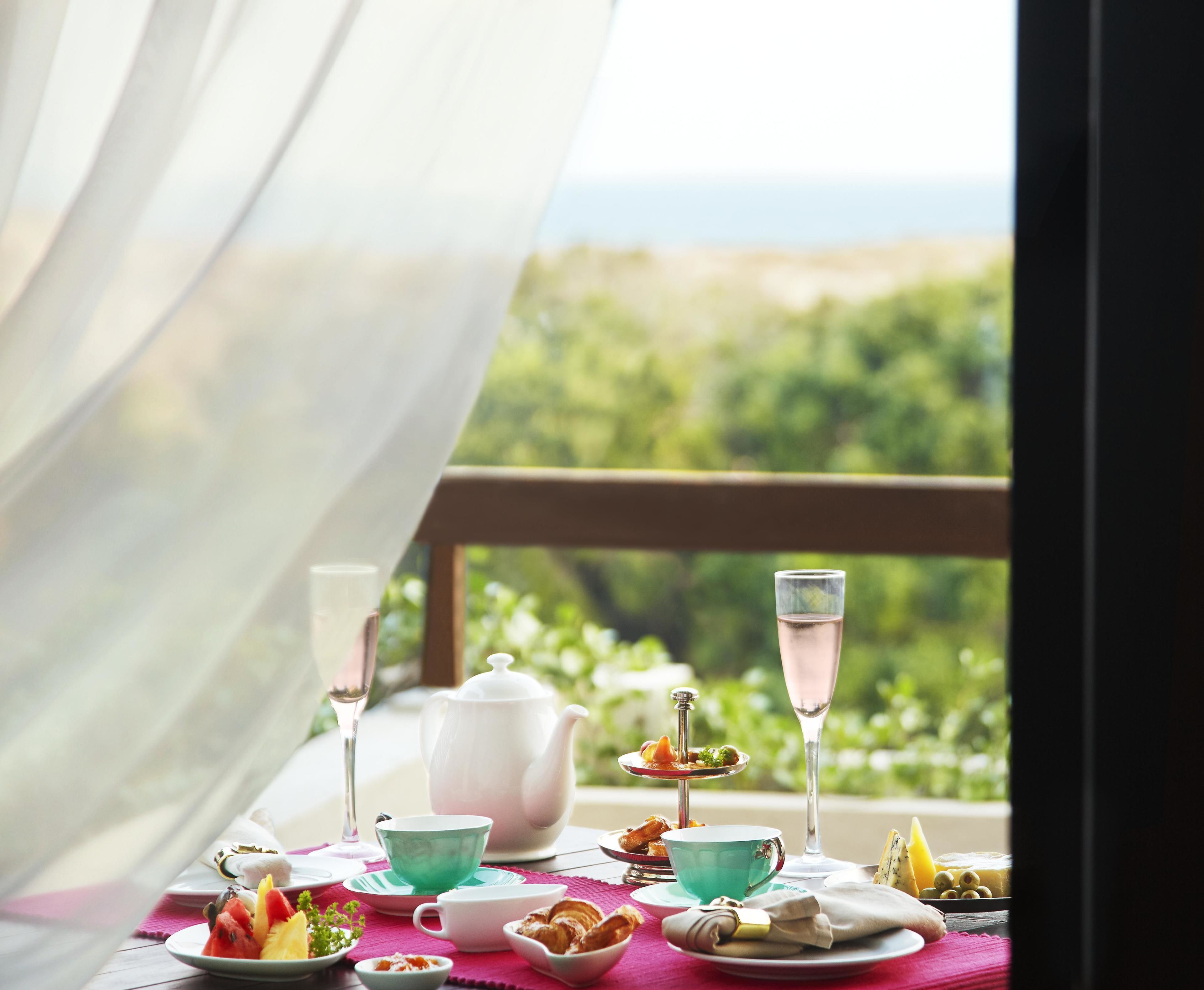 Une table dressée avec des tasses à thé, une théière et diverses collations, offrant une vue pittoresque par la fenêtre.