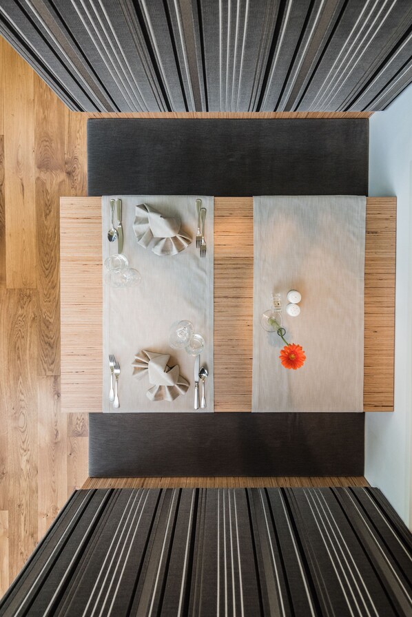 A dining table with a dark center and light edges, surrounded by wooden flooring and a dark ceiling. - Hotel Royal (Sesto)
