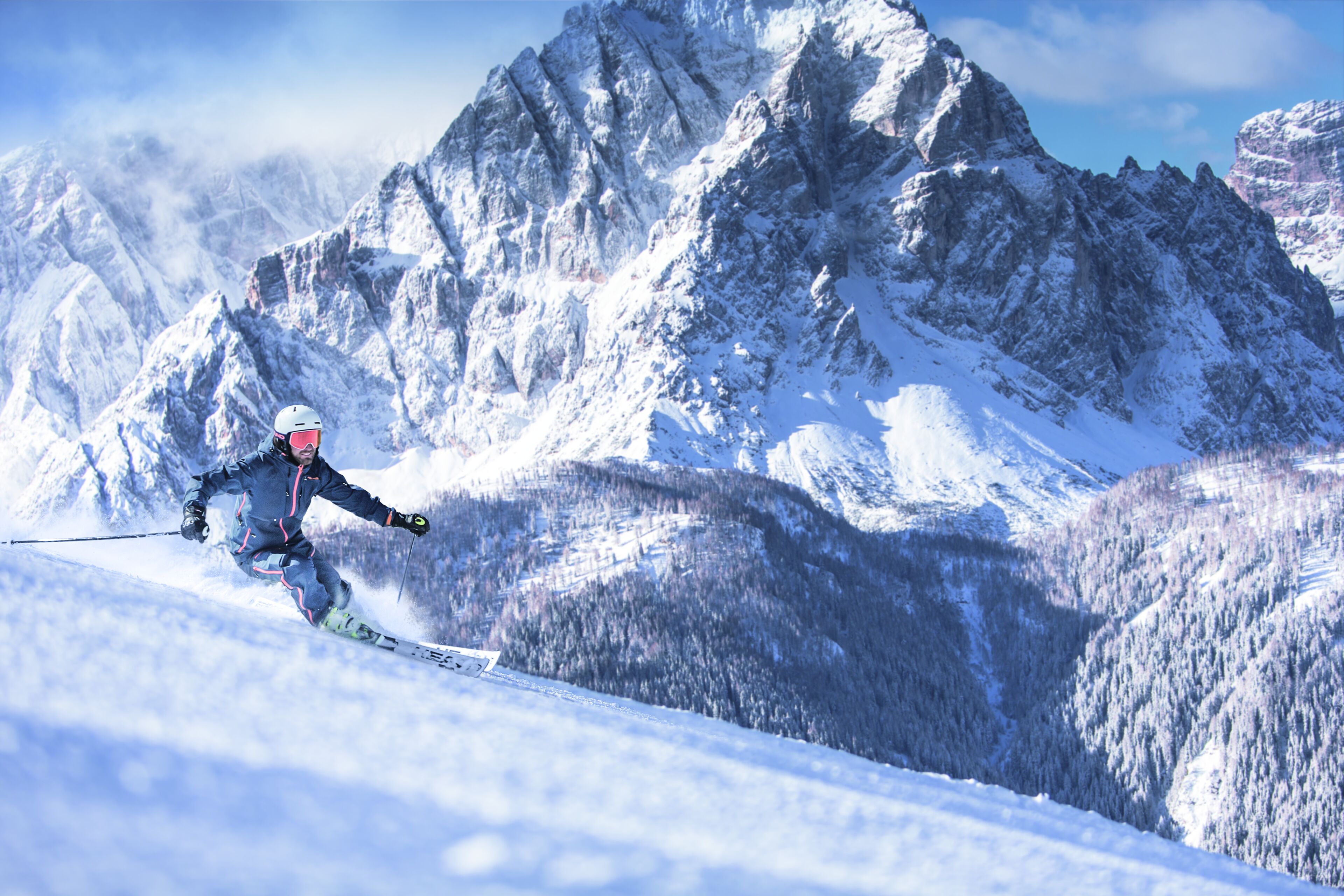 A skier on a snowy slope with a mountainous backdrop.
