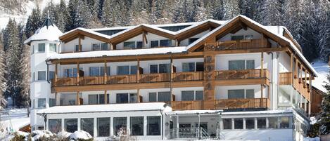 A multi-story hotel with balconies, large windows, and a ski slope in the background.