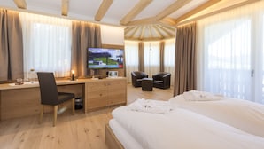 Una camera d'albergo con soffitto in legno, un letto, una scrivania con una sedia, una televisione e un'area salotto con sedie e un tavolo.