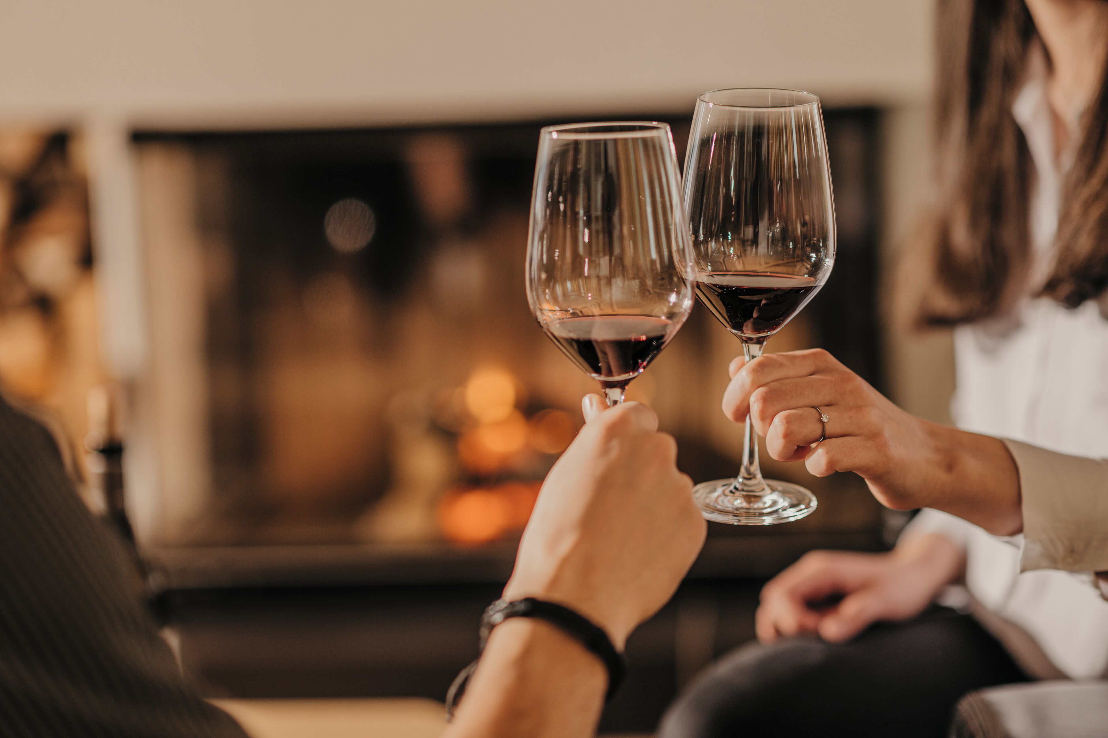Two people holding wine glasses, seated in a room with a fireplace in the background.