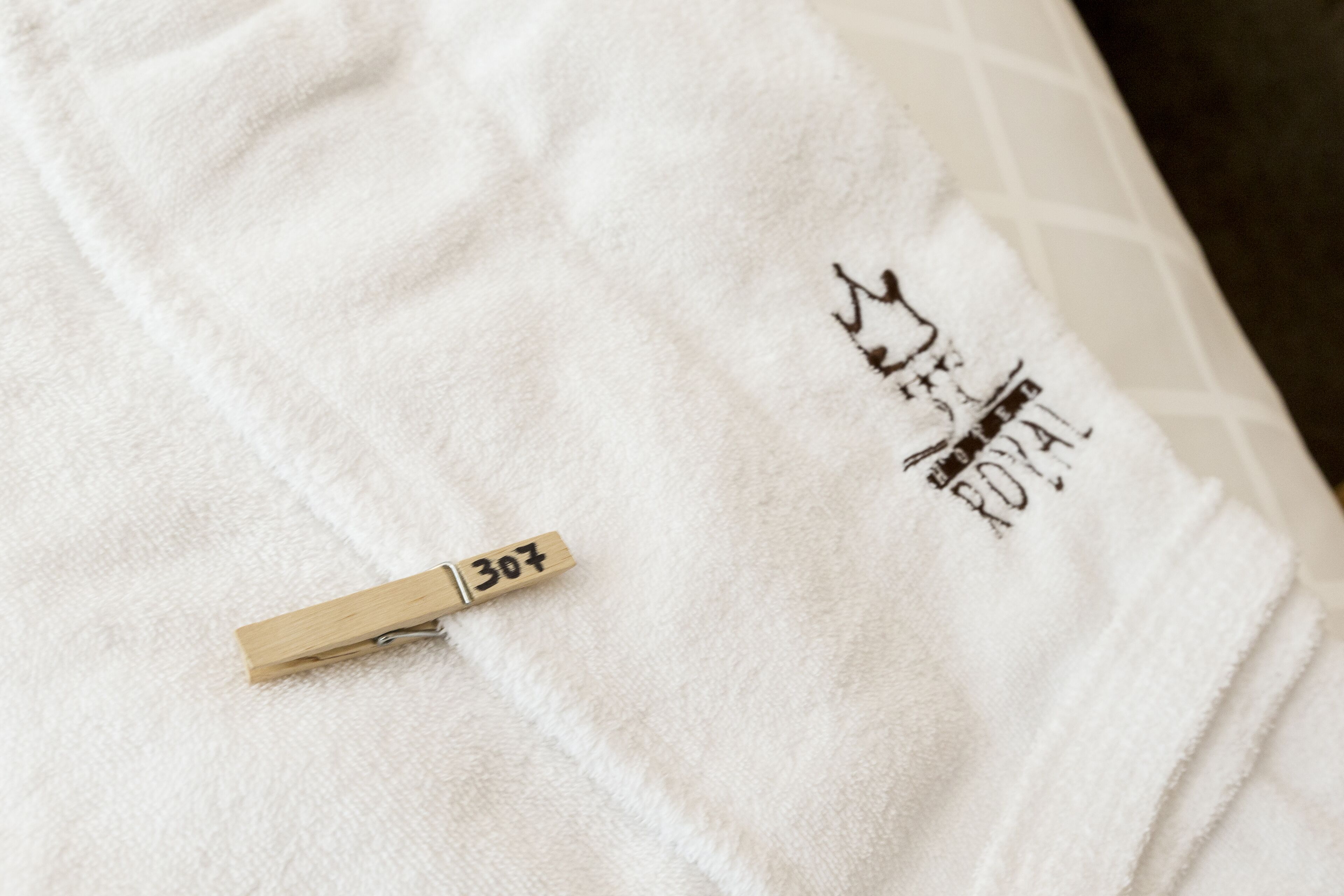 Un asciugamano bianco con una molletta di legno con l'etichetta '307' e un logo.
