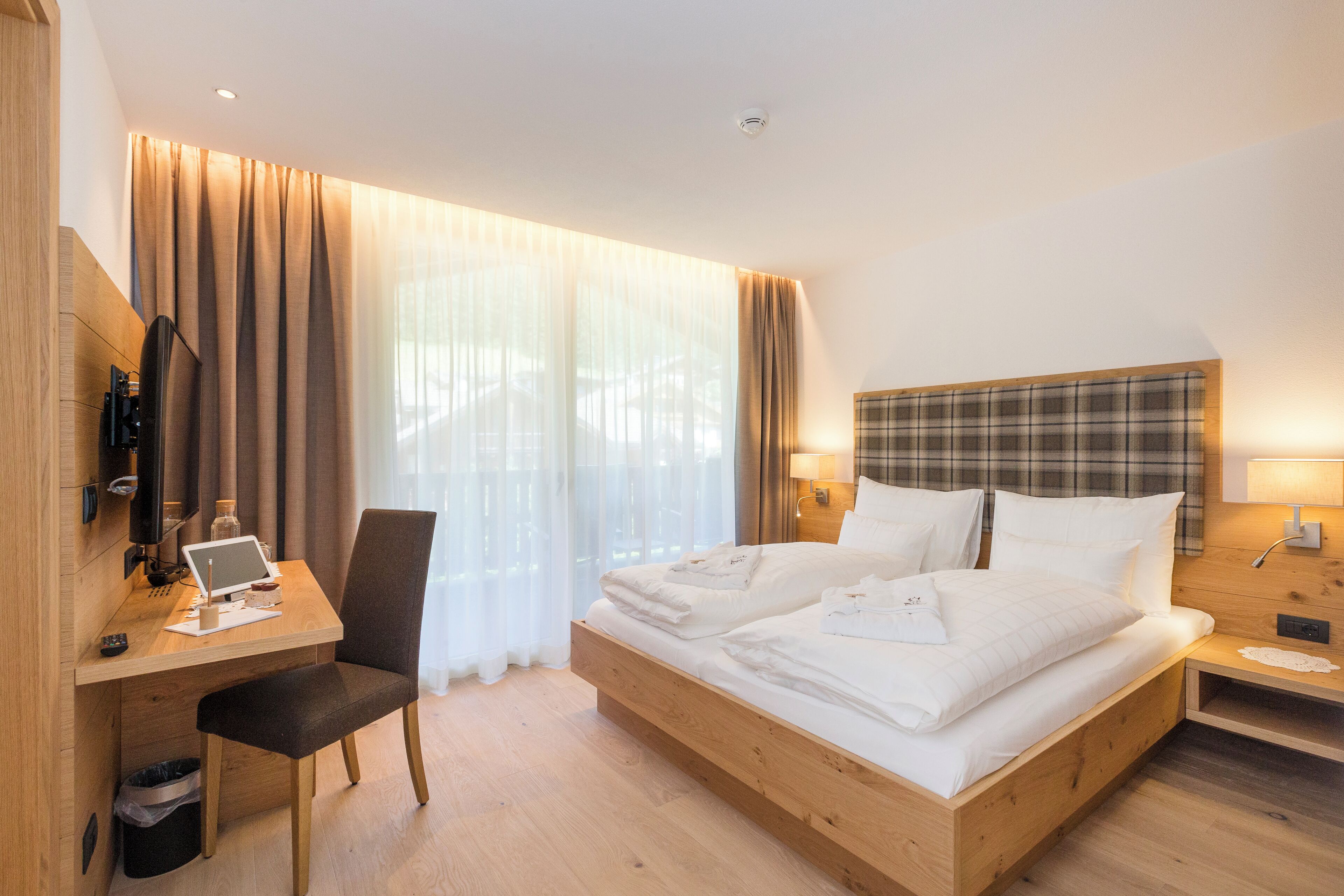 A hotel room with a wooden bed, a desk with a laptop, a chair, and a TV.