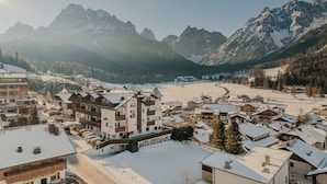 Un paese montano innevato con edifici in legno tradizionali, una pista da sci e una vista chiara delle montagne circostanti.