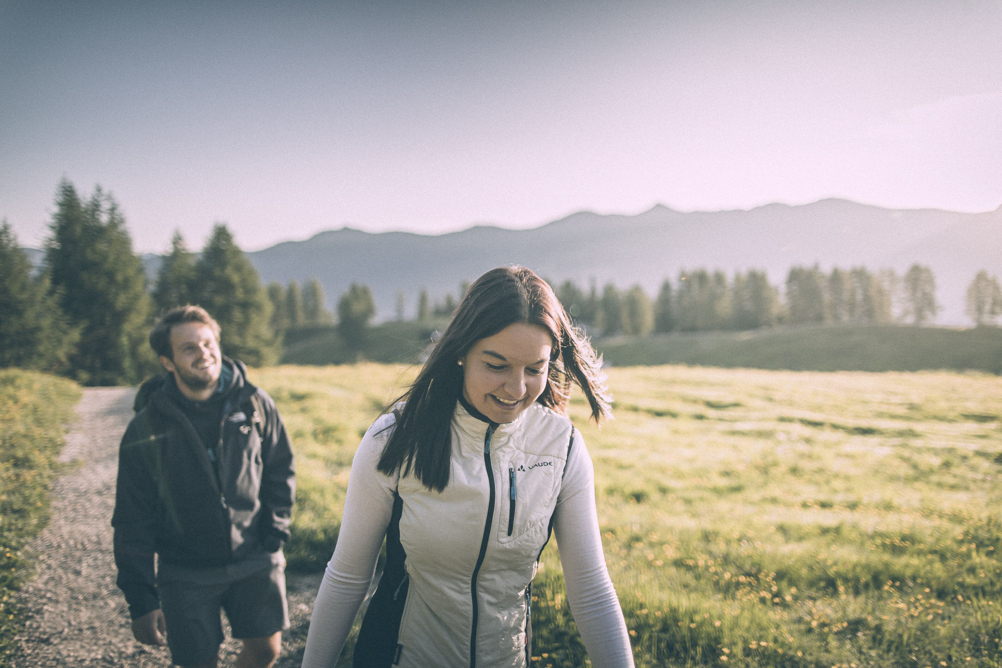 A person walking on a path in a grassy field with mountains in the background.