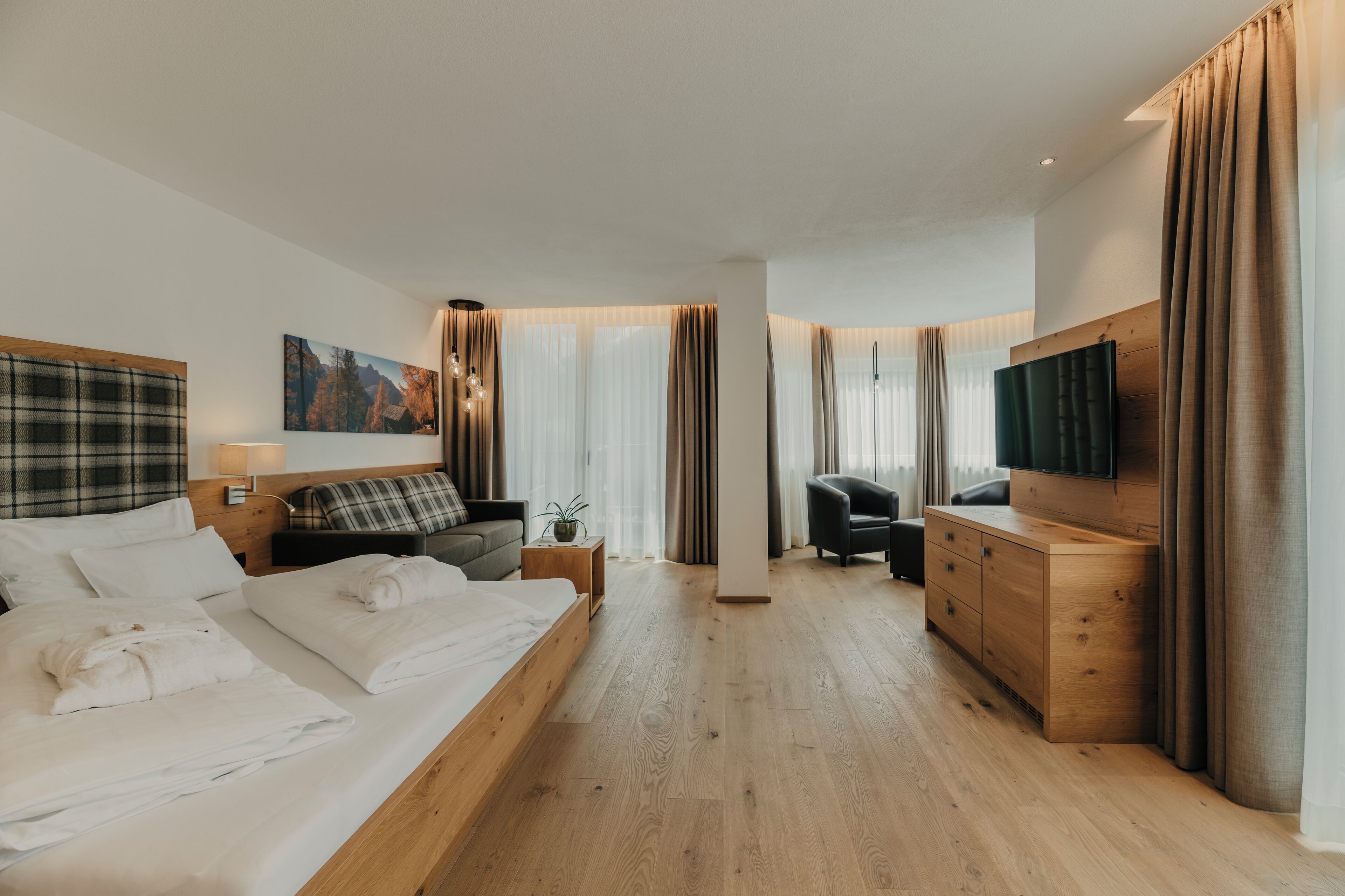 Una habitación de hotel moderna con una cama grande, un escritorio, un sofá, un televisor y un aparador de madera.