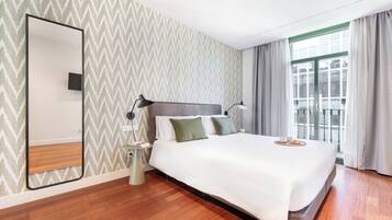 Ein modernes Hotelzimmer mit einem großen Bett, einem Nachttisch, einem Spiegel und Blick auf die Stadt durch große Fenster.