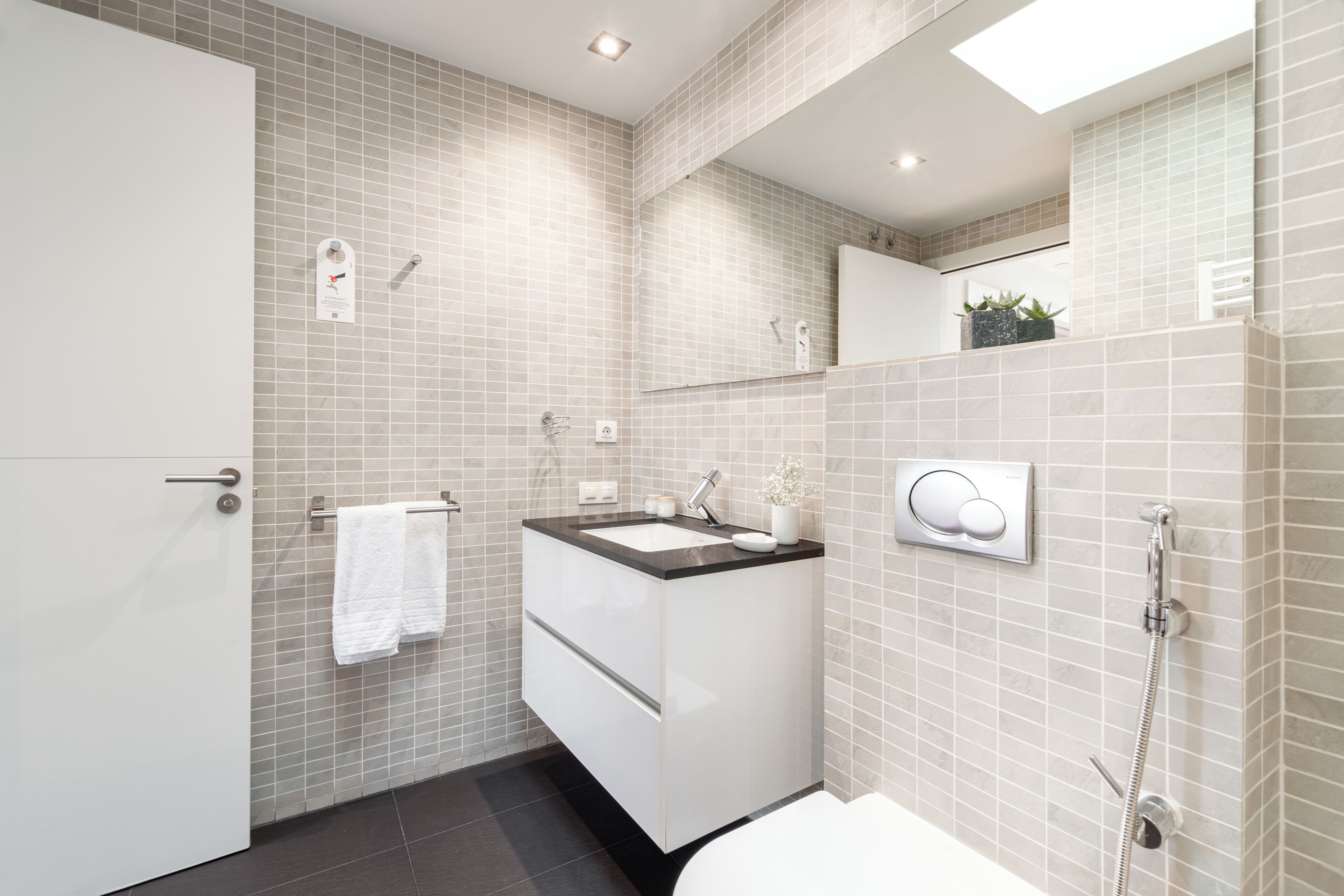 A modern bathroom with a white sink, mirror, and toilet.