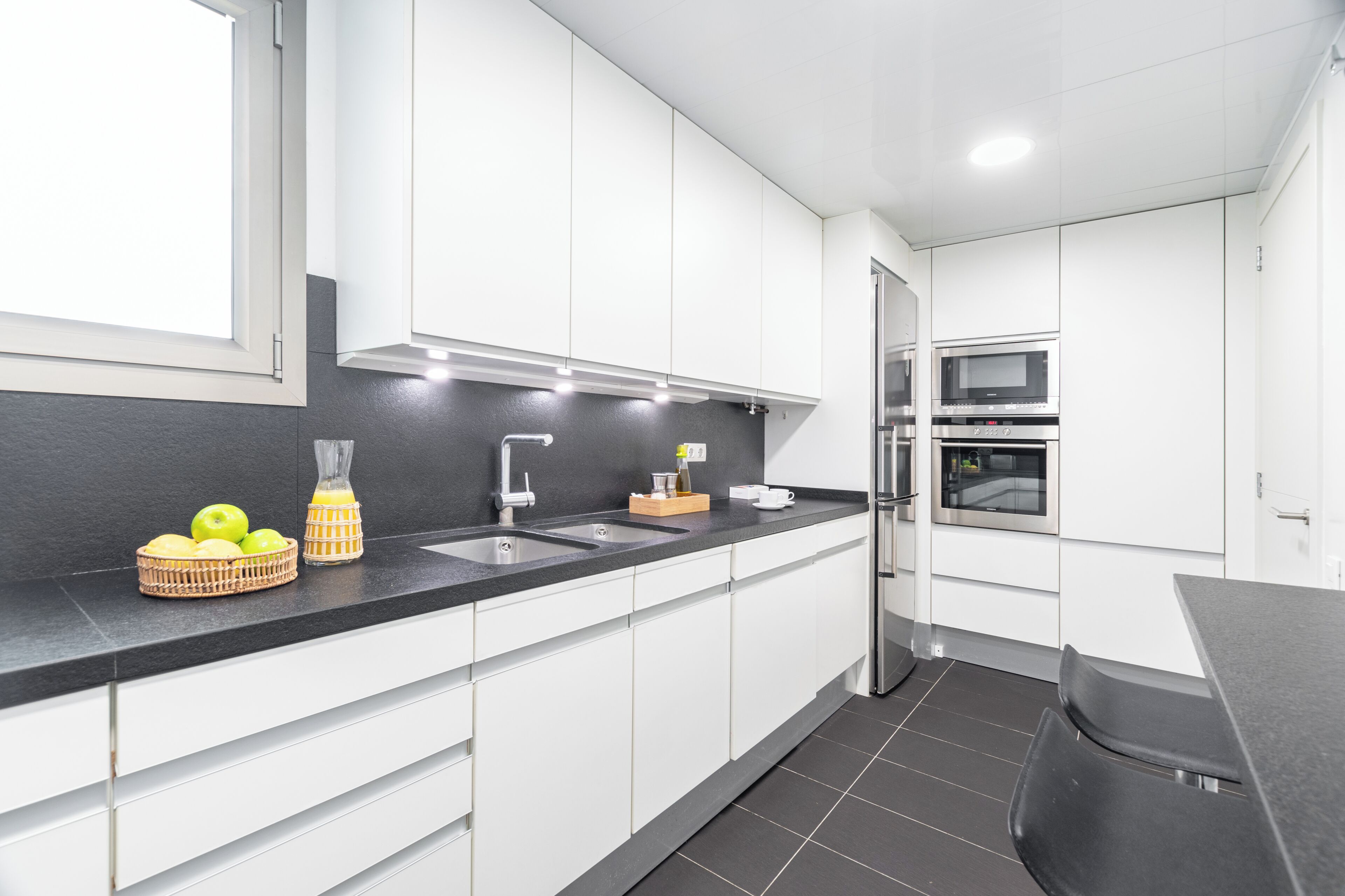 Een moderne keuken met witte kasten, een zwart aanrecht, een spoelbak, een fornuis en een koelkast.