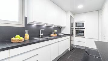 Een moderne keuken met witte kasten, een zwart aanrecht, een spoelbak, een fornuis en een koelkast.