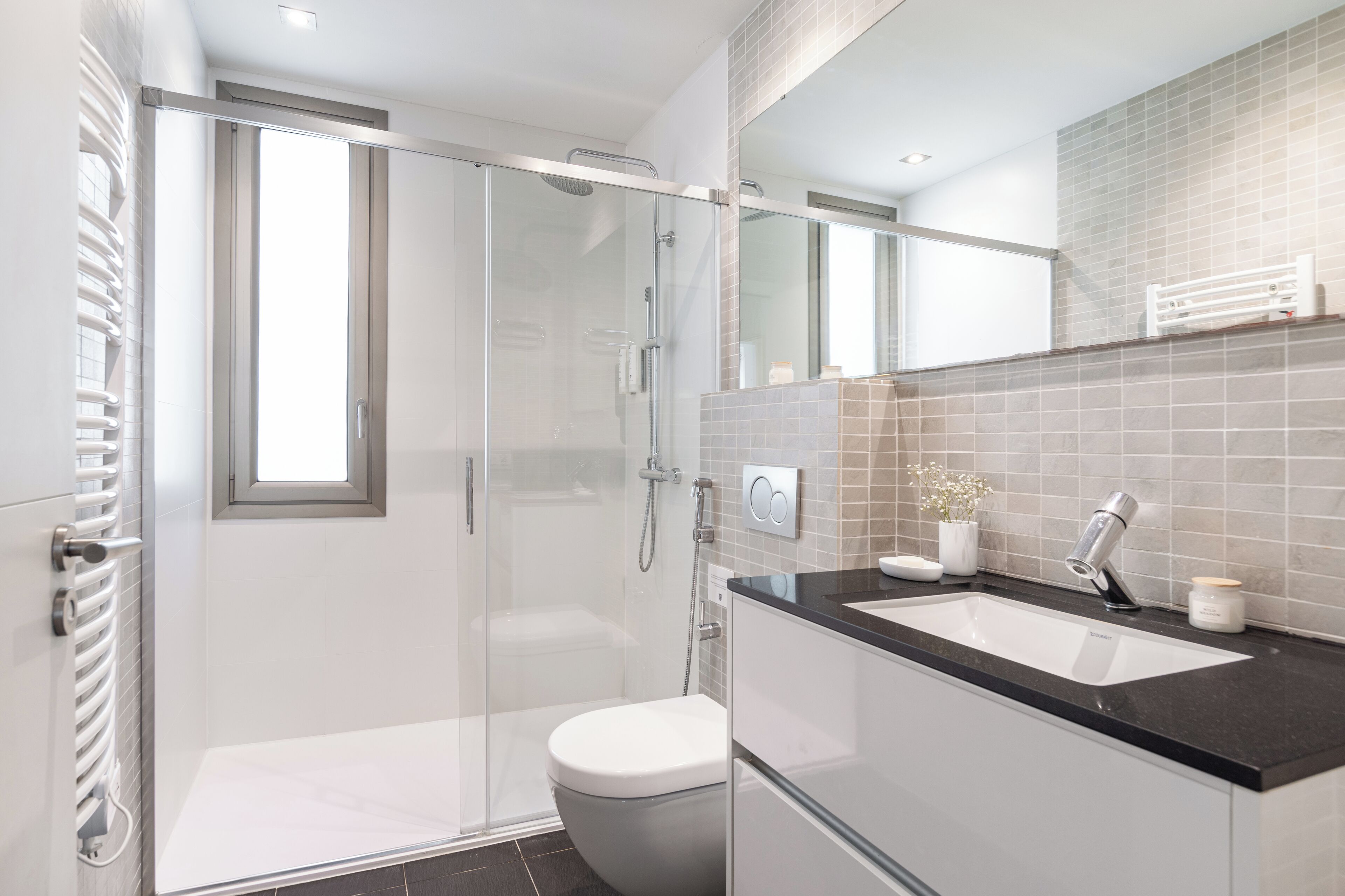 Un bagno moderno con doccia vetrata, un water bianco e un lavabo su piano nero.
