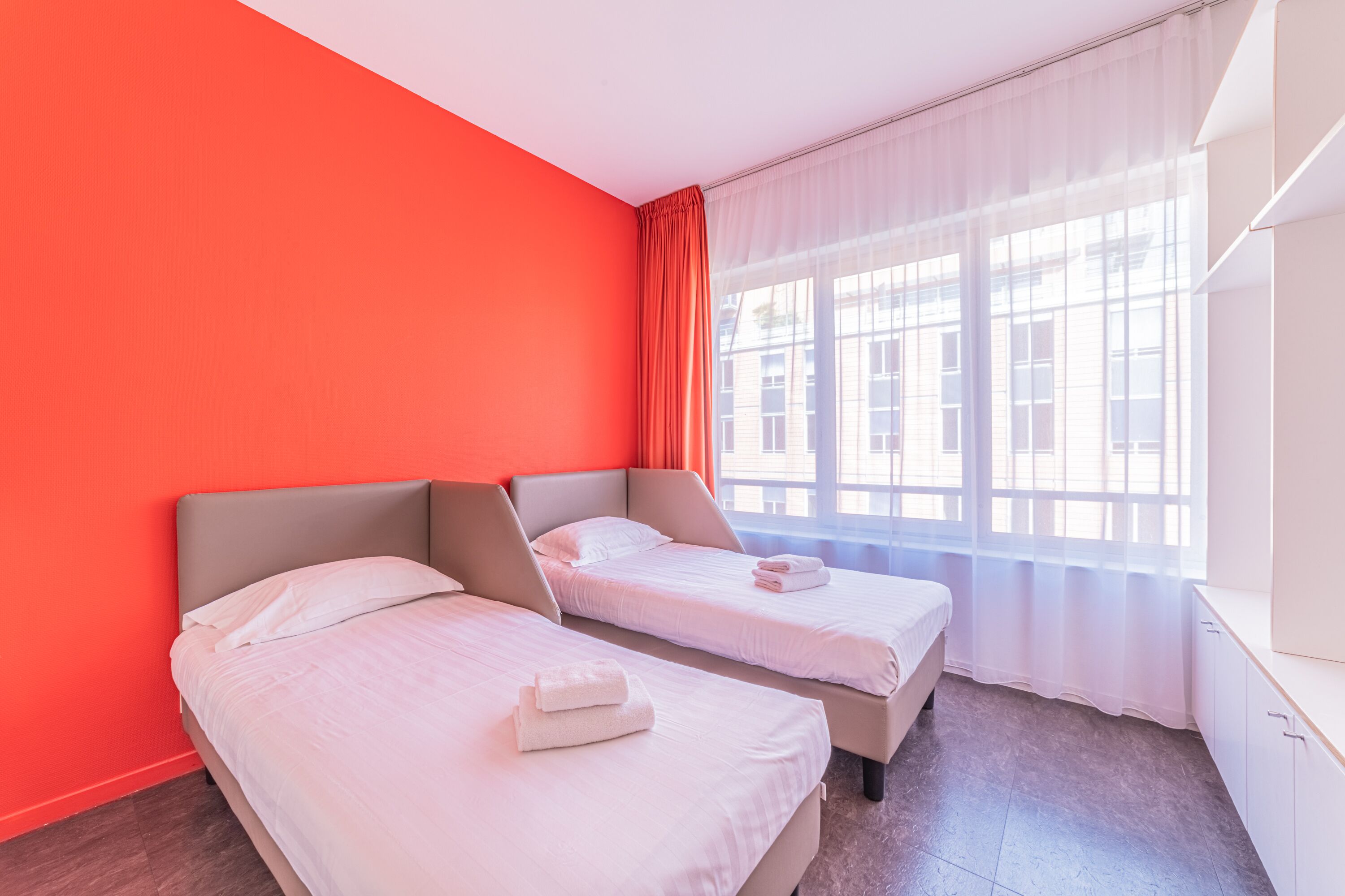 Una habitación de hotel con dos camas, un ventanal con cortinas y un armario blanco.
