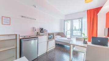 A compact, modern room with a kitchenette, a bed with a view, a desk with a laptop, and a dining area.