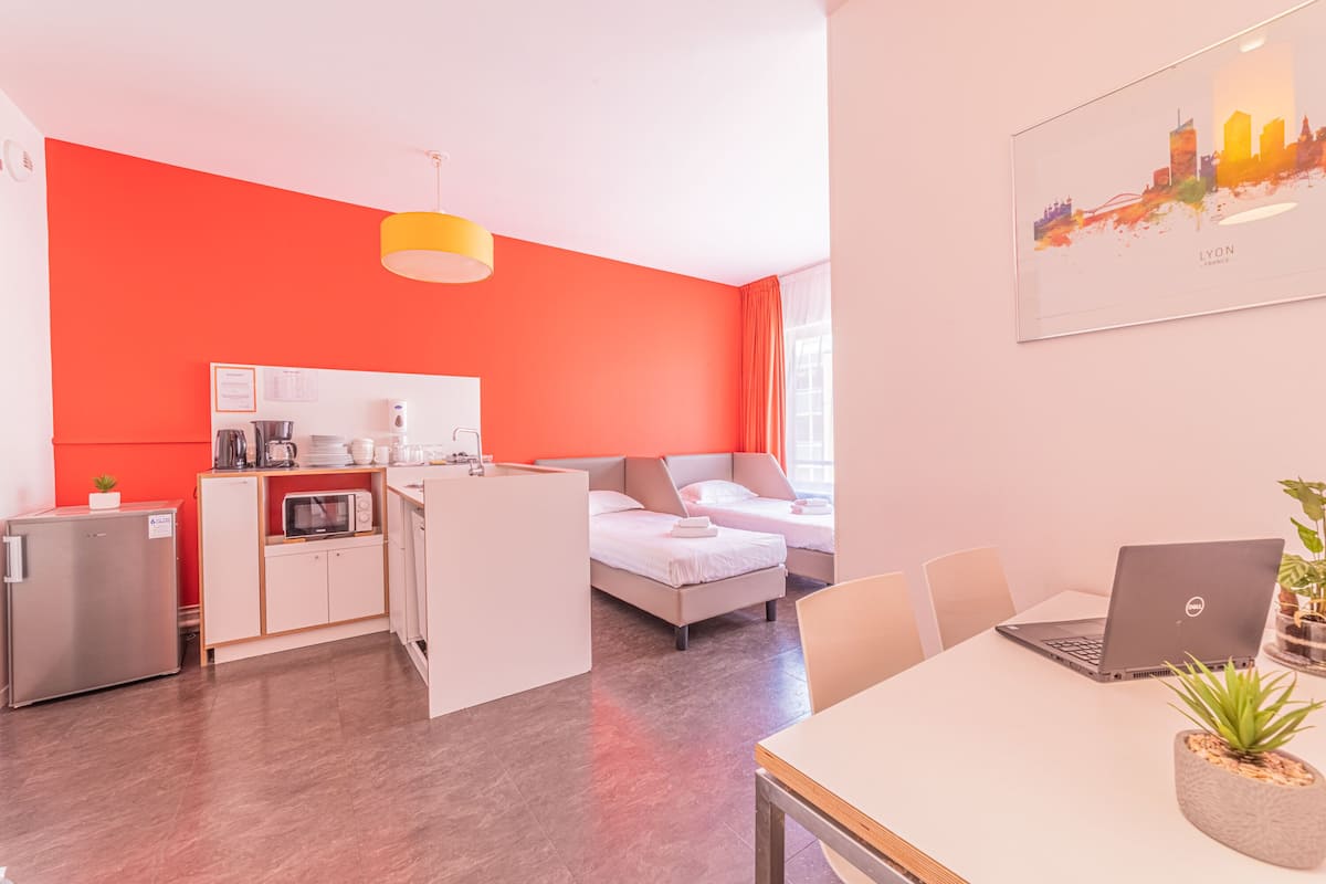 Une chambre d’hôtel moderne équipée d’une kitchenette, d’un lit, d’un coin repas et d’un tableau représentant un paysage urbain.