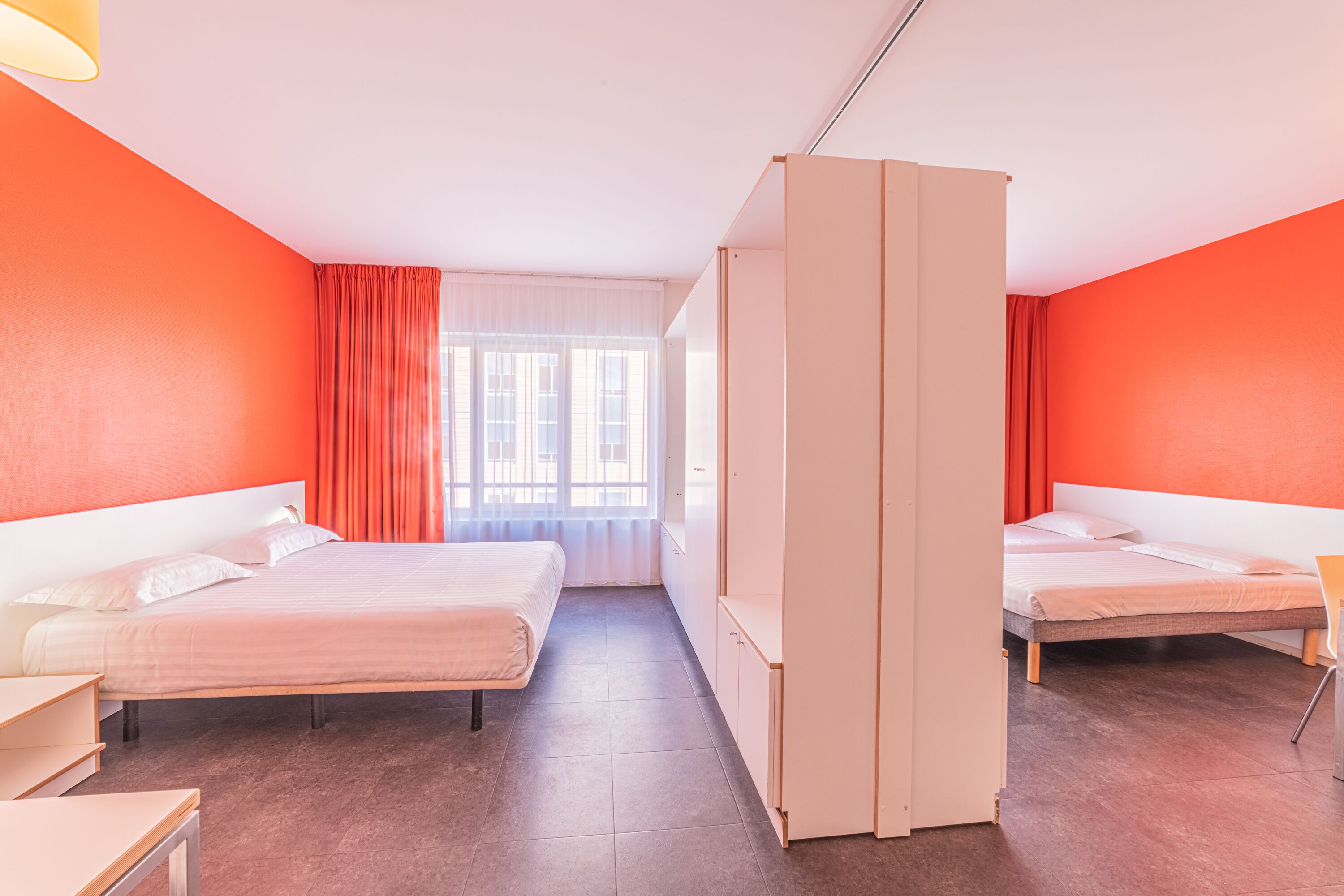 A hotel room with two beds, a wardrobe, and a window with curtains.