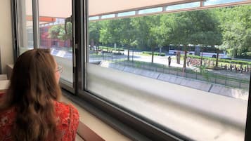 A person sitting by a window overlooking a plaza with trees and a bus.
