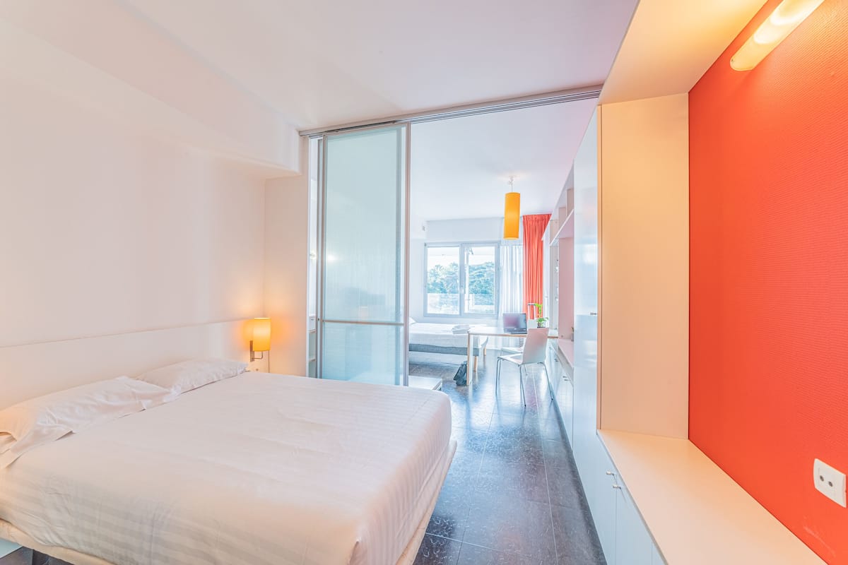 Une chambre d’hôtel moderne, équipée d’un lit, d’un bureau et offrant une vue à travers une porte vitrée.