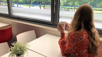 Une personne est assise à une table, devant une fenêtre donnant sur un parc où sont garés des vélos.