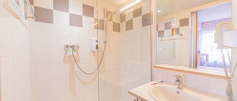 A modern bathroom with a glass-enclosed shower, a sink with a mirror, and a telephone.
