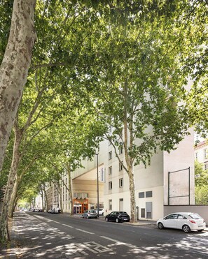 A tree-lined street with a modern building featuring a flat facade and multiple windows. - Montempô Lyon Part Dieu (Lyon)