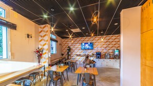 Un café moderno con varias mesas y sillas de madera, un televisor en la pared y una máquina de café.