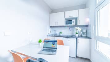 A modern kitchen with white cabinets, a microwave, and a dishwasher. There's a laptop on a table with a glass and a plant.