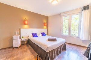 A hotel room with a large bed, a nightstand, a suitcase, and a window with curtains.