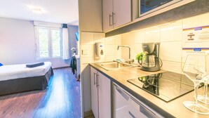 Una habitación de hotel compacta con kitchenette, una cama, un ventanal con cortinas y vistas al exterior.