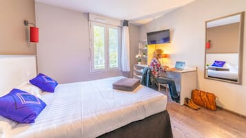 A hotel room with a bed, a desk with a computer, a TV, and a window with curtains.