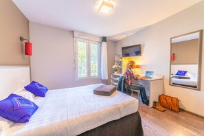 A hotel room with a bed, a desk with a computer, a TV, and a window with curtains. - Montempô Lyon Part Dieu (Lyon)