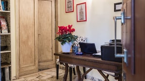 A wooden door, a desk with a laptop, a vase with red flowers, and framed pictures on the wall. - Soggiorno Fortezza Fiorentina (Florence)