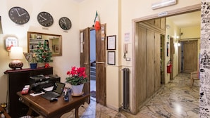 A hotel lobby with clocks showing different cities, a reception desk, a Christmas tree, and a hallway leading to rooms. - Soggiorno Fortezza Fiorentina (Florence)