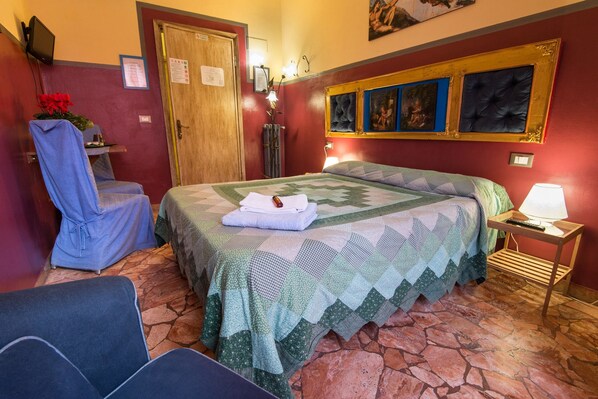 A hotel room with a bed, a chair, a desk with a lamp, and a painting on the wall. - Soggiorno Fortezza Fiorentina (Florence)