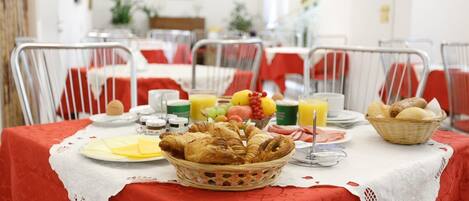A breakfast setting with a table set for two, featuring croissants, fruits, and beverages.