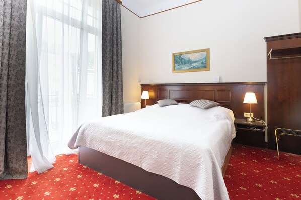 Una habitación de hotel con una cama grande, dos lámparas de noche, un cuadro en la pared y una alfombra roja.