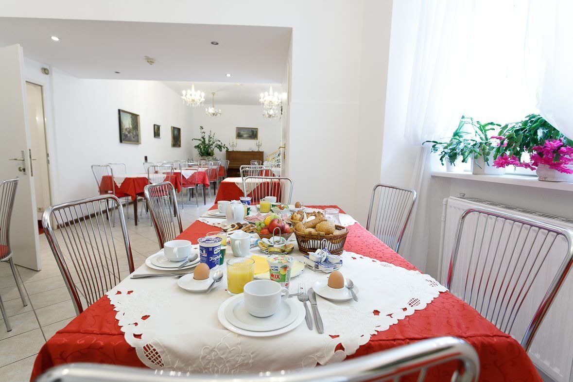 Un comedor con una mesa lista para el desayuno, con platos, tazas y una cesta de frutas.