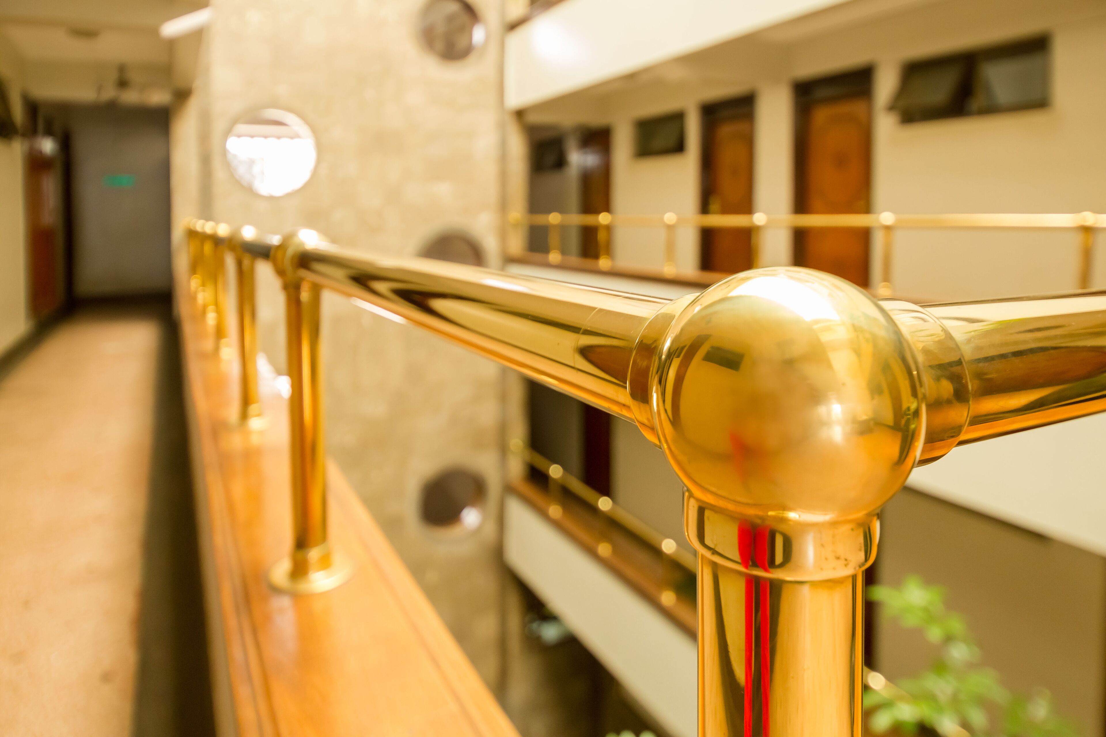 Um corredor com corrimão dourado, parede de mármore e reflexo de um trem.
