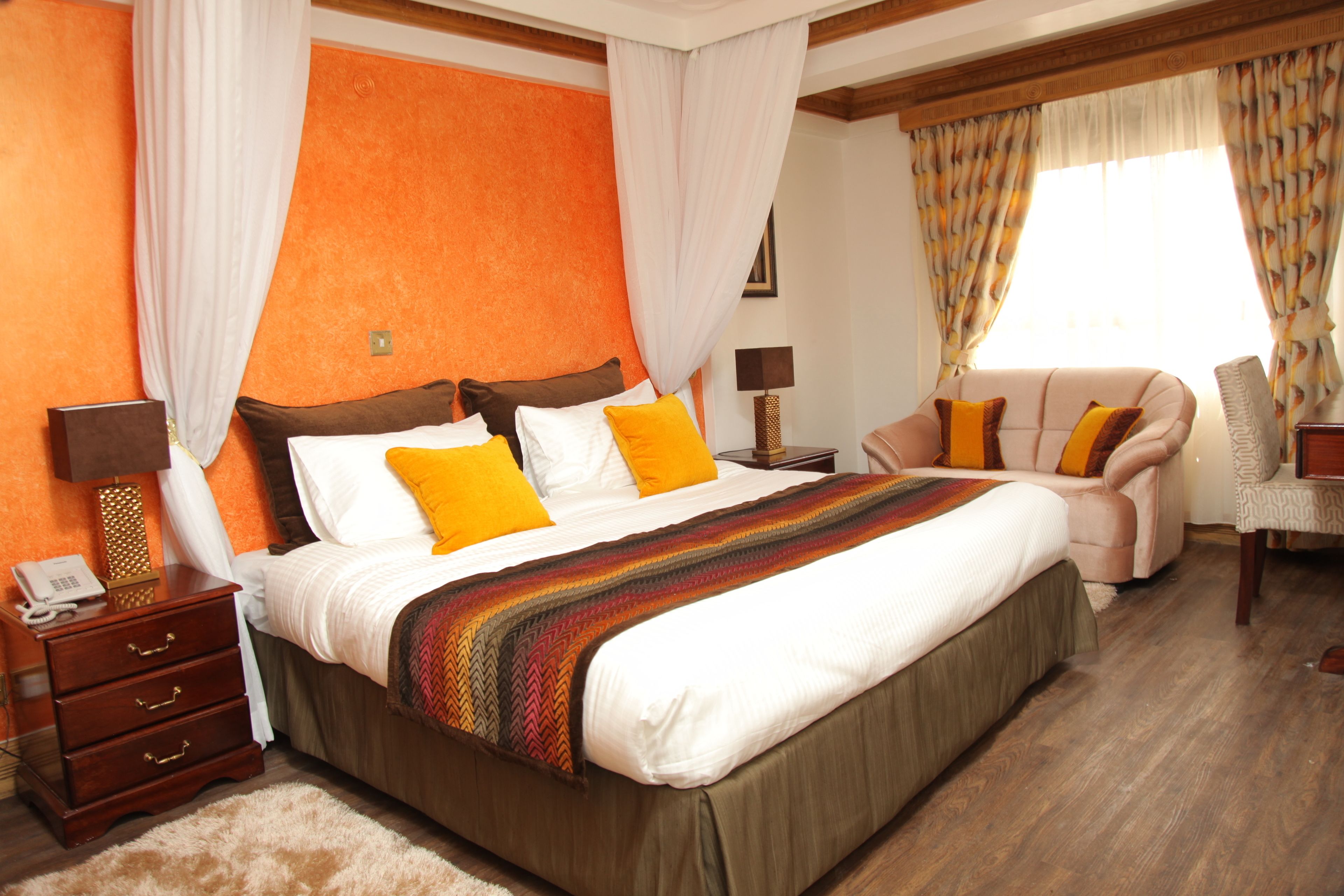 Une chambre d’hôtel avec un grand lit, une table de chevet avec une lampe, une chaise et une fenêtre avec des rideaux.