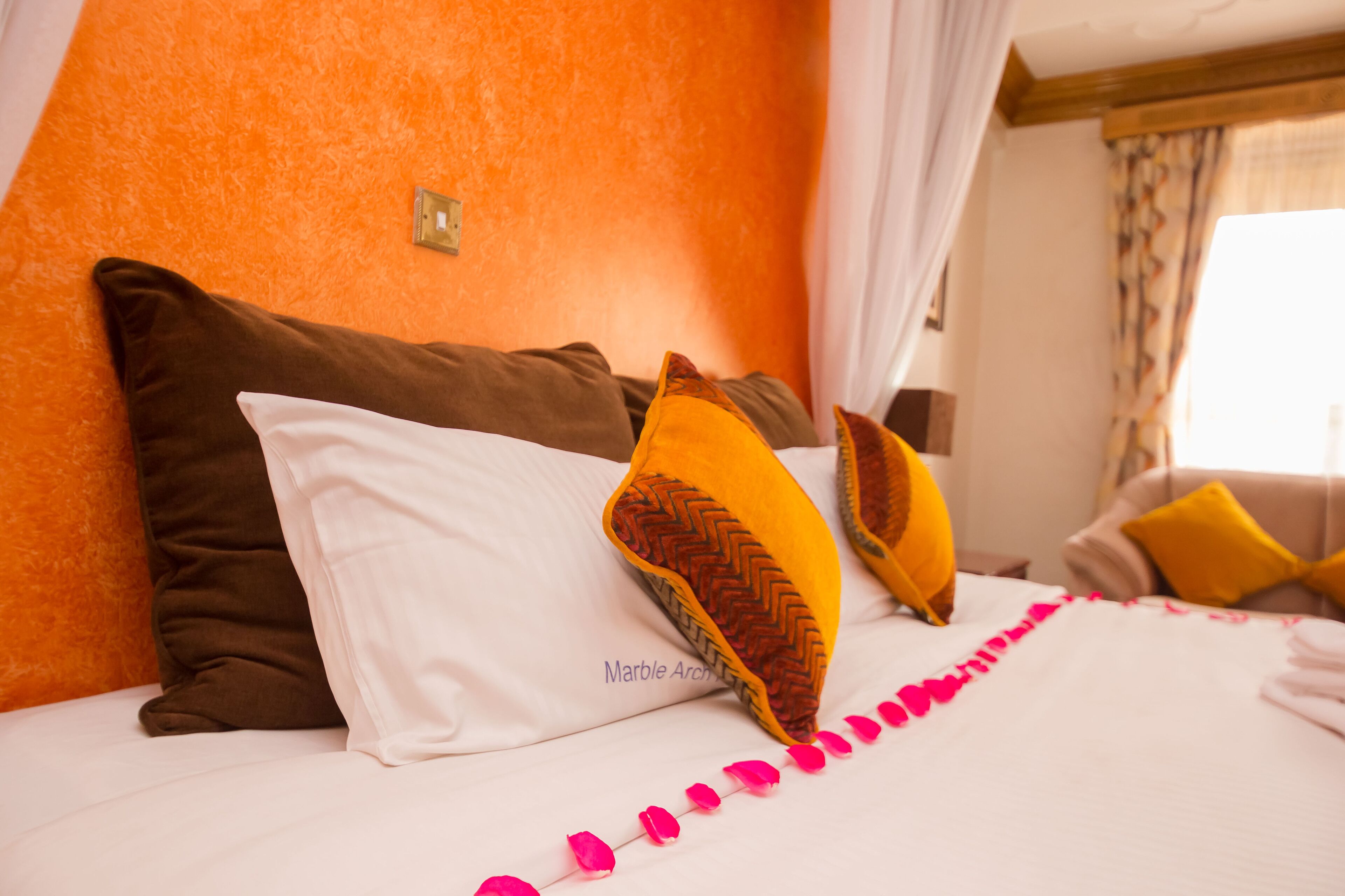 Cama com almofadas brancas e castanhas, um detalhe rosa decorativo e um arco de mármore.