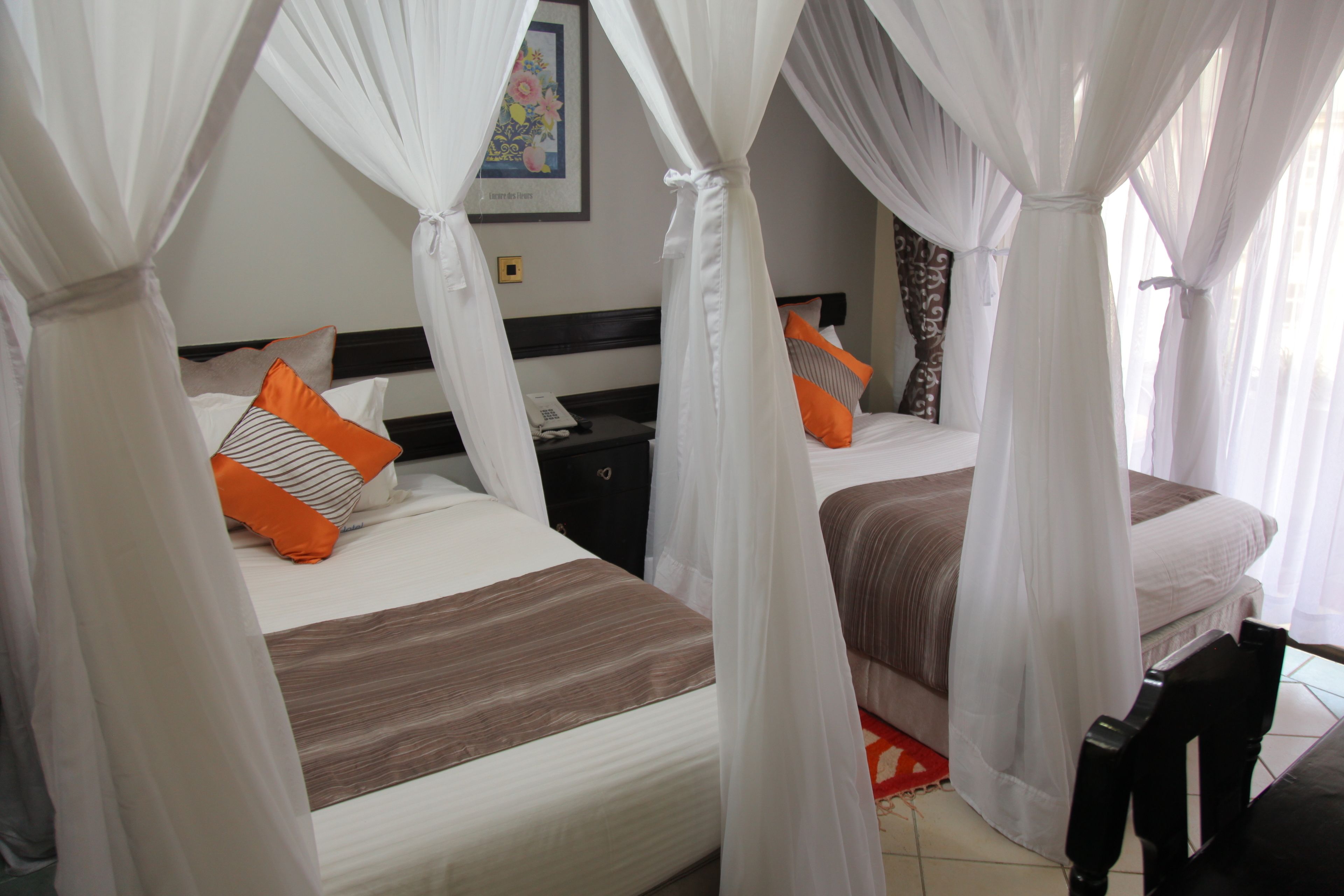A hotel room with two beds, each with a canopy bedspread and pillows. There is a nightstand with a phone and a small table between the beds.