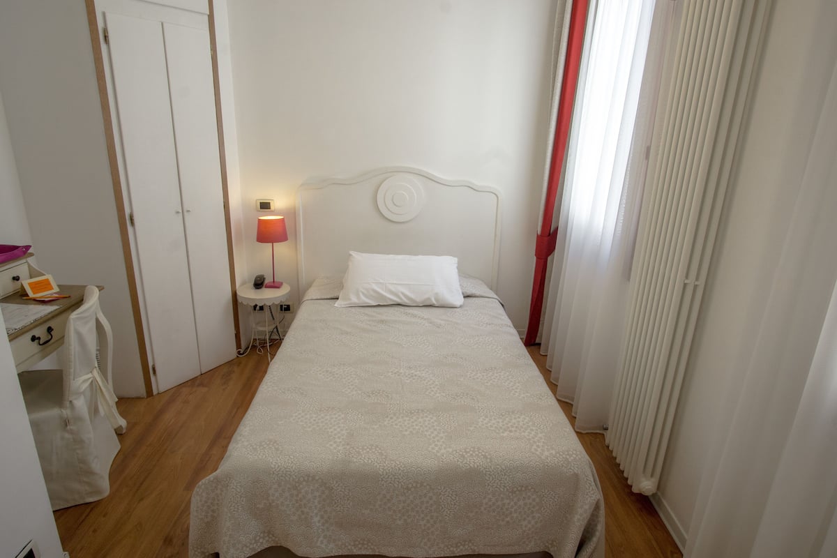 A neatly made bed with a white headboard, a bedside table with a lamp, and a window with curtains.