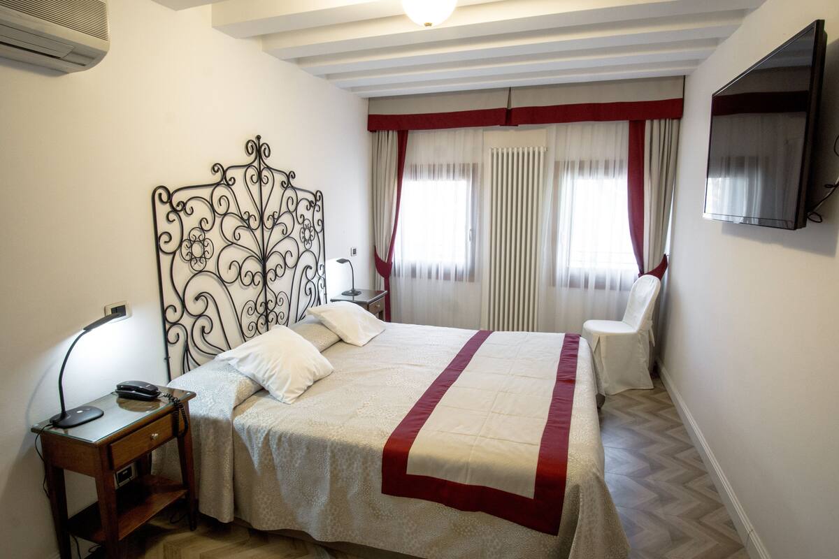 A bedroom with a bed, bedside table, lamp, and a TV mounted on the wall.