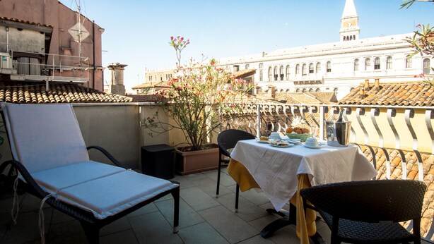 Una terraza con una mesa y sillas, una planta en maceta y un edificio con una torre del reloj al fondo.