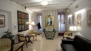 Un salón luminoso con una araña, sillas a rayas, un sofá negro y un espejo sobre un aparador.