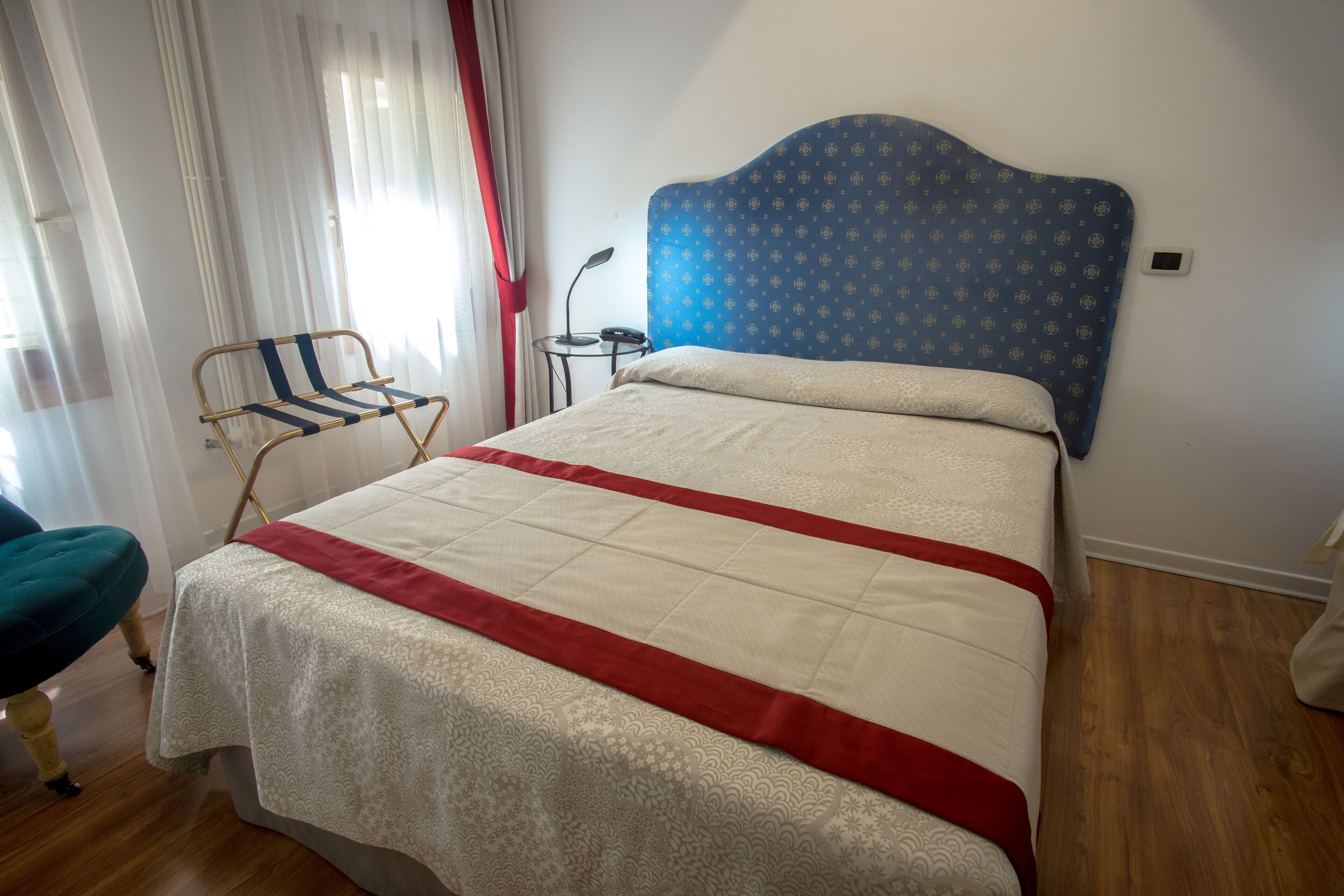 A neatly made bed with a patterned headboard, a bedside table with a lamp, and a chair with a cushion.