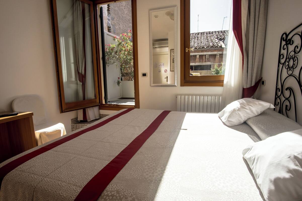 A bedroom with a large bed, a mirror, a desk, and a view of the outside.