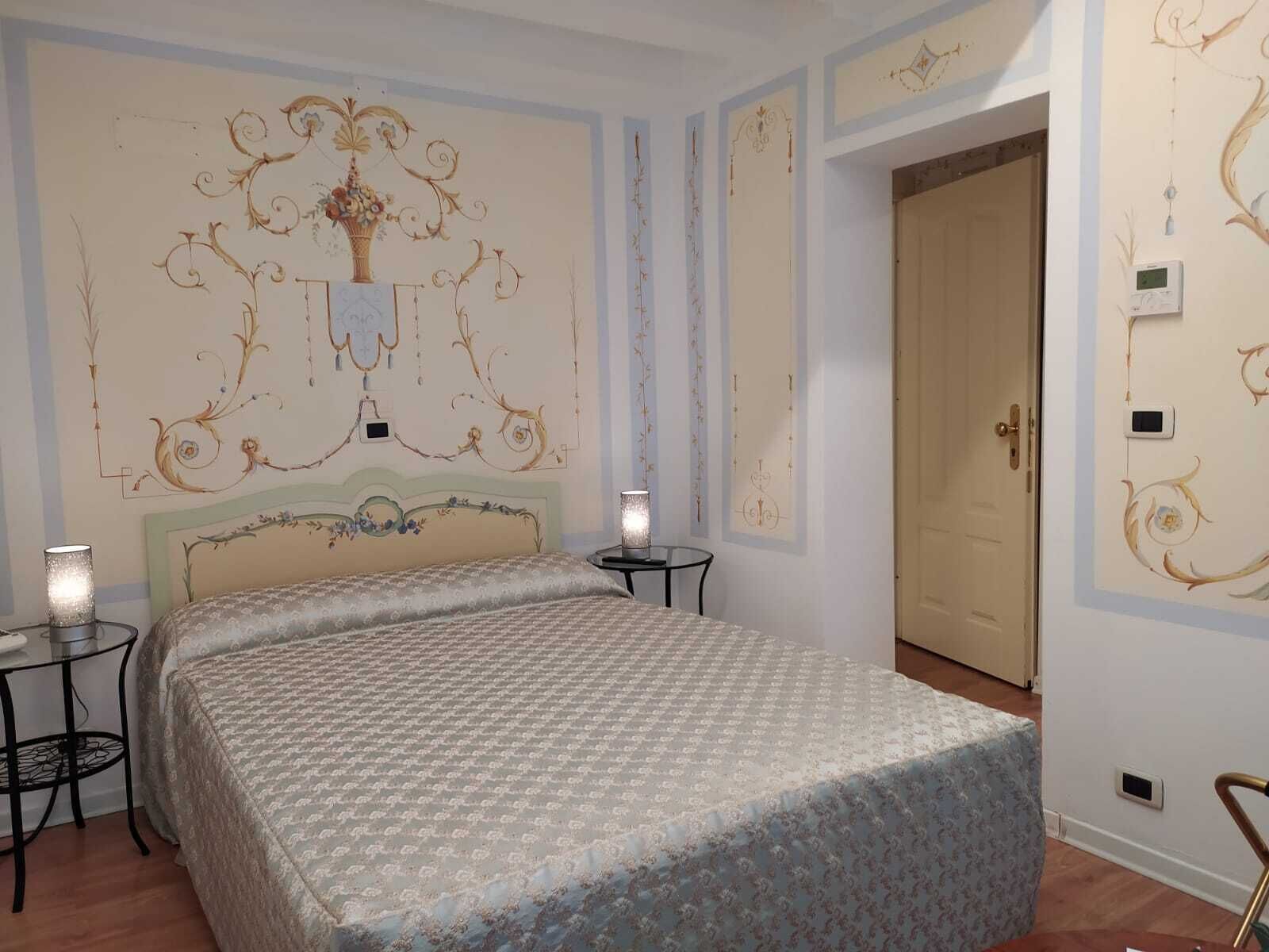 A bedroom with a bed, two bedside tables, a wall with ornate designs, and a door.